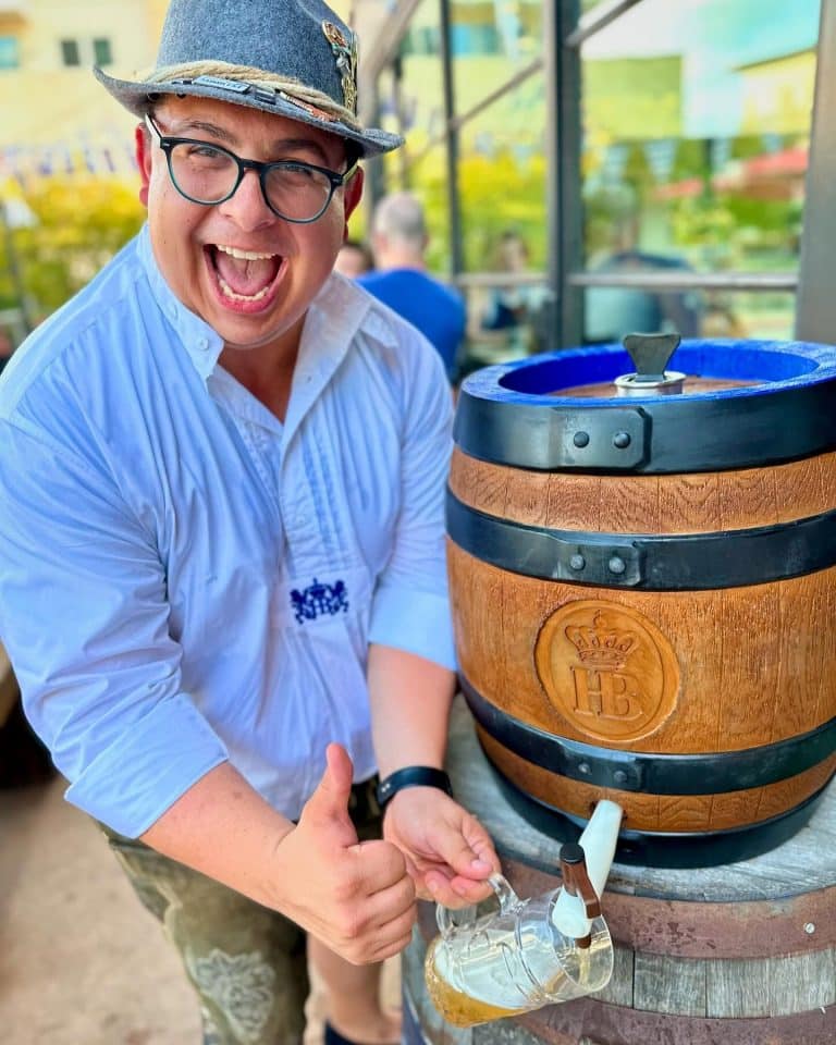 A man pouring a beer from a wooden Hofbräuhaus keg into a glass stein during a local Las Colinas Oktoberfest event.