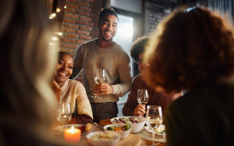 Happy African American people talking to their friends while enjoying in dinner at dining room.